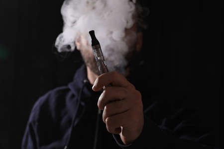 Man using electronic cigarette against black background, focus on handの写真素材