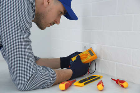 Professional electrician with tester checking voltage indoors
