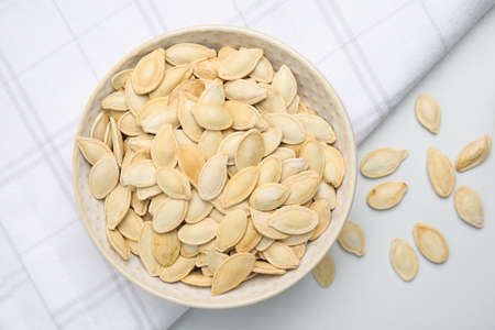 Bowl with pumpkin seeds on light table, flat lay