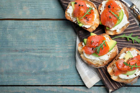 Delicious sandwiches with cream cheese, salmon, avocado and arugula served on light blue wooden...