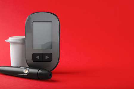 Digital glucometer, lancet pen and container on red background, space for text. diabetes control