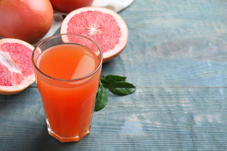 Tasty freshly made grapefruit juice on blue wooden table. Space for textの写真素材