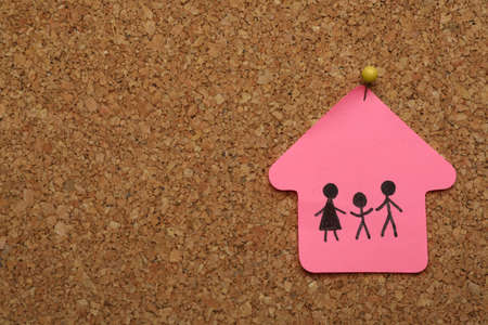House shaped note with drawing of family pinned to cork board, space for text. child adoption conceptの写真素材