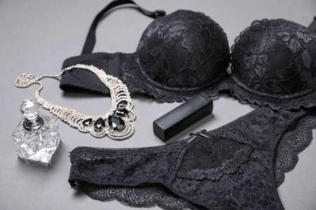 Elegant black women's underwear, perfume, lipstick and necklace on gray backgroundの写真素材