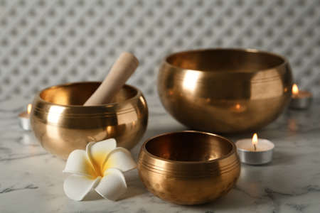 Tibetan singing bowls, mallet, plumeria flower and burning candles on white marble tableの写真素材
