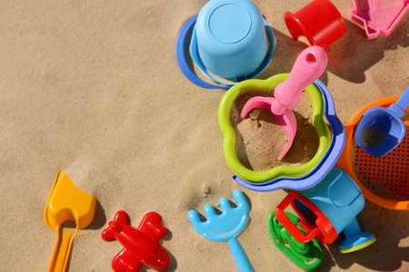 Set of plastic beach toys on sand, flat lay with space or text. outdoor play