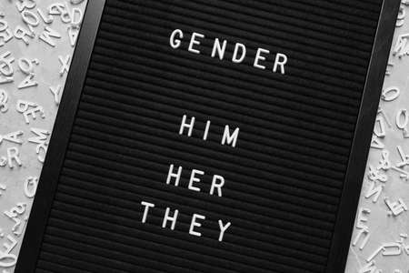 Black board with words Gender, Him, Her, They and letters on gray marble table, flat lay
