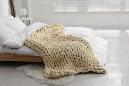 Soft chunky knit blanket on bed in stylish room interior