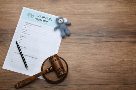 Adoption application, gavel, toy bear and pen on wooden table, flat lay. Space for text
