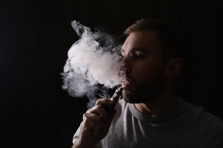 Man using electronic cigarette on black backgroundの写真素材