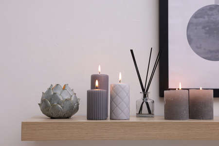 Burning candles and air freshener on wooden shelf indoorsの写真素材