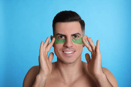 Man applying green under eye patches on light blue background