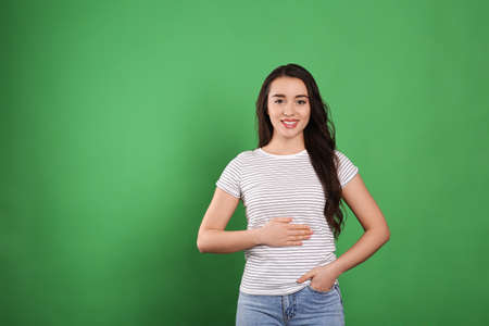 Happy healthy woman touching her belly on green background, space for text