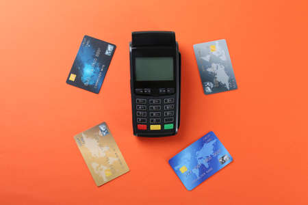New modern payment terminal and credit cards on orange background, flat layの写真素材