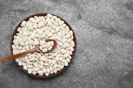 Raw white beans and spoon in bowl on wooden table, top view. Space for text