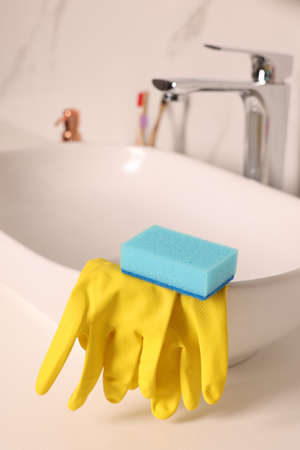 Sponge and rubber gloves on bathroom sink indoors