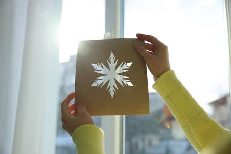 Woman holding snowflake stencil near window at home, closeupの写真素材