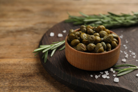 Bowl of capers, salt and rosemary on wooden table, space for textの写真素材