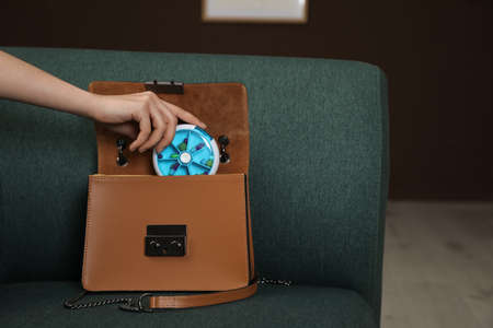 Woman plastic box with pills into bag on sofa indoors, closeup. Space for text
