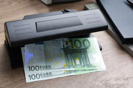 Modern currency detector with Euro banknotes on wooden table. money examination deviceの写真素材
