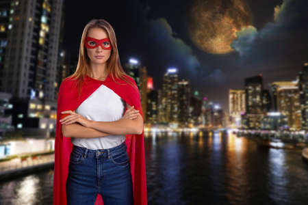 Confident woman wearing superhero costume and beautiful cityscape in the night on backgroundの写真素材