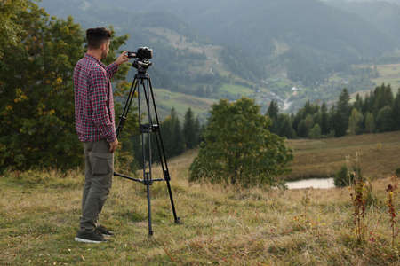 Man filming video with modern camera on tripod outdoors. Space for text