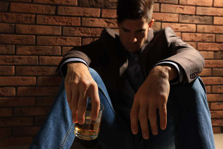 Addicted man near red brick wall, focus on glass of alcoholic drinkの写真素材