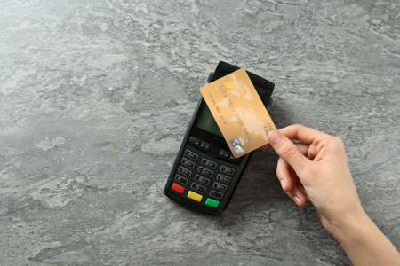 Woman with credit card using modern payment terminal at gray table, top view