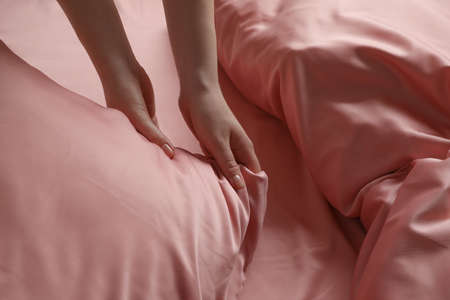 Woman making bed with beautiful pink silk linens, closeup viewの写真素材