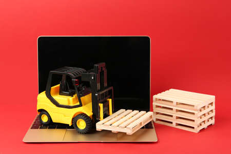 Laptop, toy forklift and wooden pallets on red backgroundの写真素材