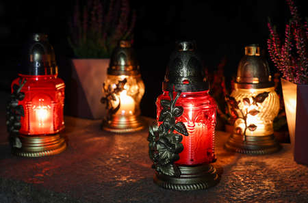 Different grave lanterns with burning candles on stone surface at night