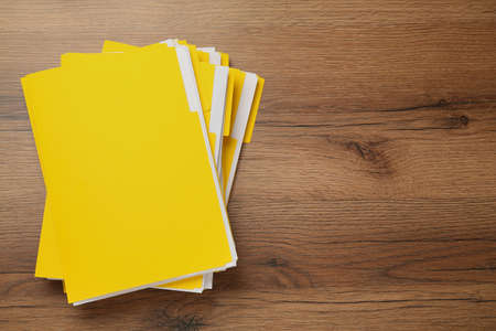 Yellow files with documents on wooden table, top view. Space for text