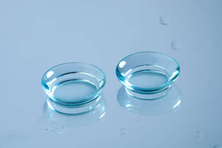 Pair of contact lenses on wet light blue reflective surfaceの写真素材