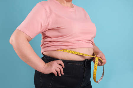 Overweight woman measuring waist with tape on light blue background, closeupの写真素材