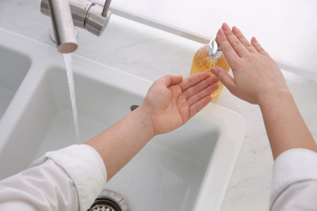 Woman washing hands with liquid soap at home, closeup
