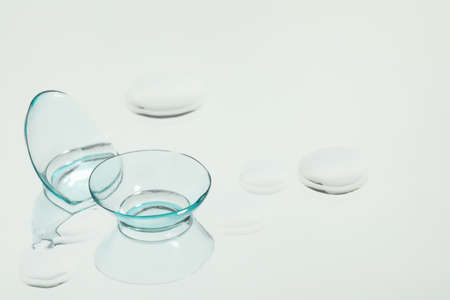 Contact lenses and drops of water on white reflective surface. Space for text