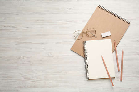 Sketchbooks, pencils, glasses and eraser on white wooden table. Space for text