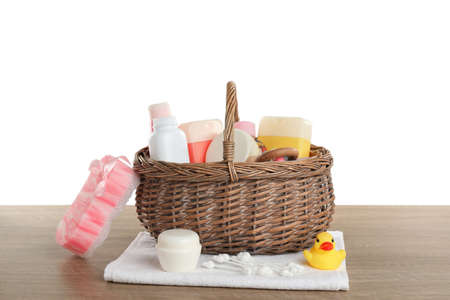 Wicker basket full of different baby cosmetic products, bathing accessories and toys on wooden table against white backgroundの写真素材