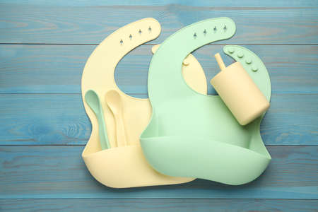 Flat lay composition with silicone baby bibs and plastic dishware on light blue wooden backgroundの写真素材