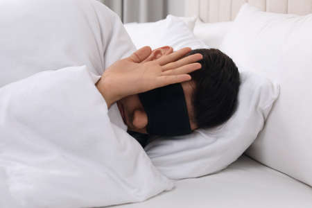 Man wearing sleeping mask in bed at homeの写真素材