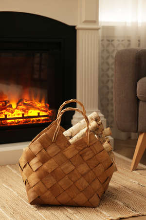 Wicker basket with wood near fireplace in roomの写真素材