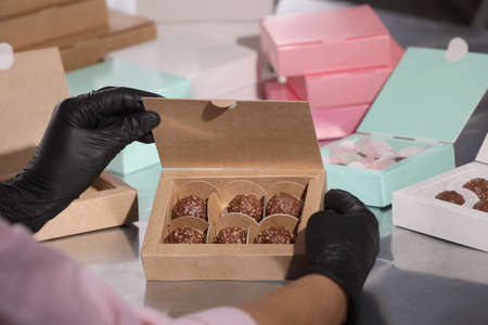 Woman packing delicious candies into box at production line, closeup