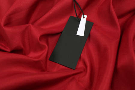 Blank black tag on red fabric. Space for textの写真素材