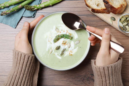 Woman eating delicious asparagus soup on wooden table, top viewの写真素材