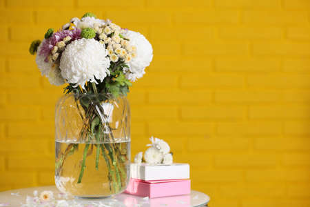 Bouquet of beautiful chrysanthemum flowers and boxes on white table against yellow brick wall, space for textの写真素材