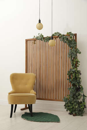 Stylish photo zone with wooden screen, floral decor and comfortable armchair indoorsの写真素材
