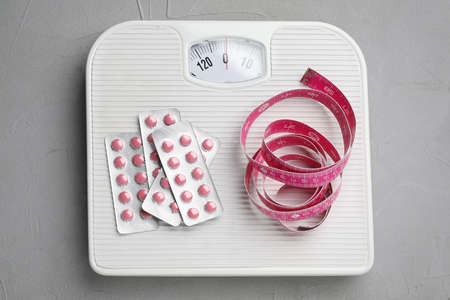 Scales with weight loss pills and measuring tape on gray table, top viewの写真素材