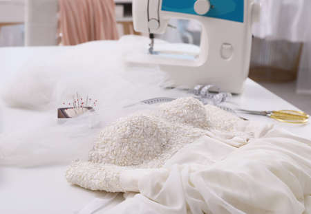 Beautiful wedding dress with embroidered bustline on table in dressmaking workshopの写真素材