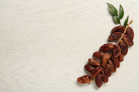 Branch of sweet dried dates and green leaves on white wooden table, top view. Space for textの写真素材