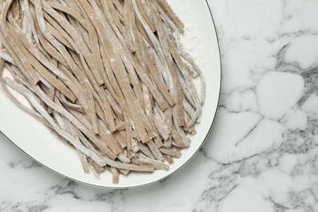 Uncooked homemade soba (buckwheat noodles) on white marble table, top viewの写真素材